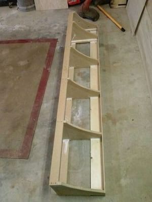 A long wooden shelf is sitting on a concrete floor next to a broom.