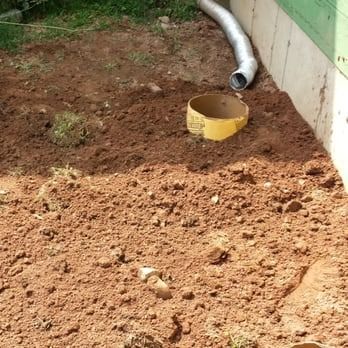 A yellow bucket is sitting in the dirt next to a pipe.