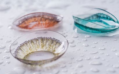 Three colored contact lenses in clear plastic packaging, wet surface.