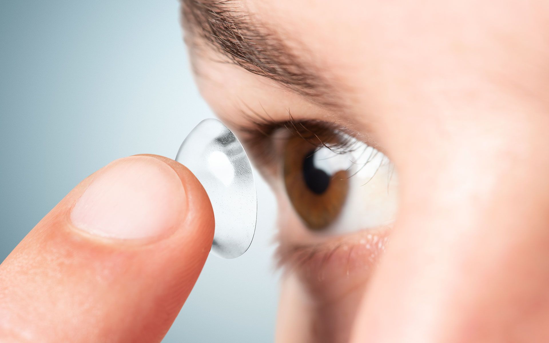 Person inserting a contact lens into their brown eye.