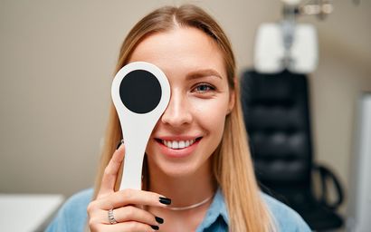 Woman at eye exam, covering one eye with a paddle, smiling. Interior, clinic setting.