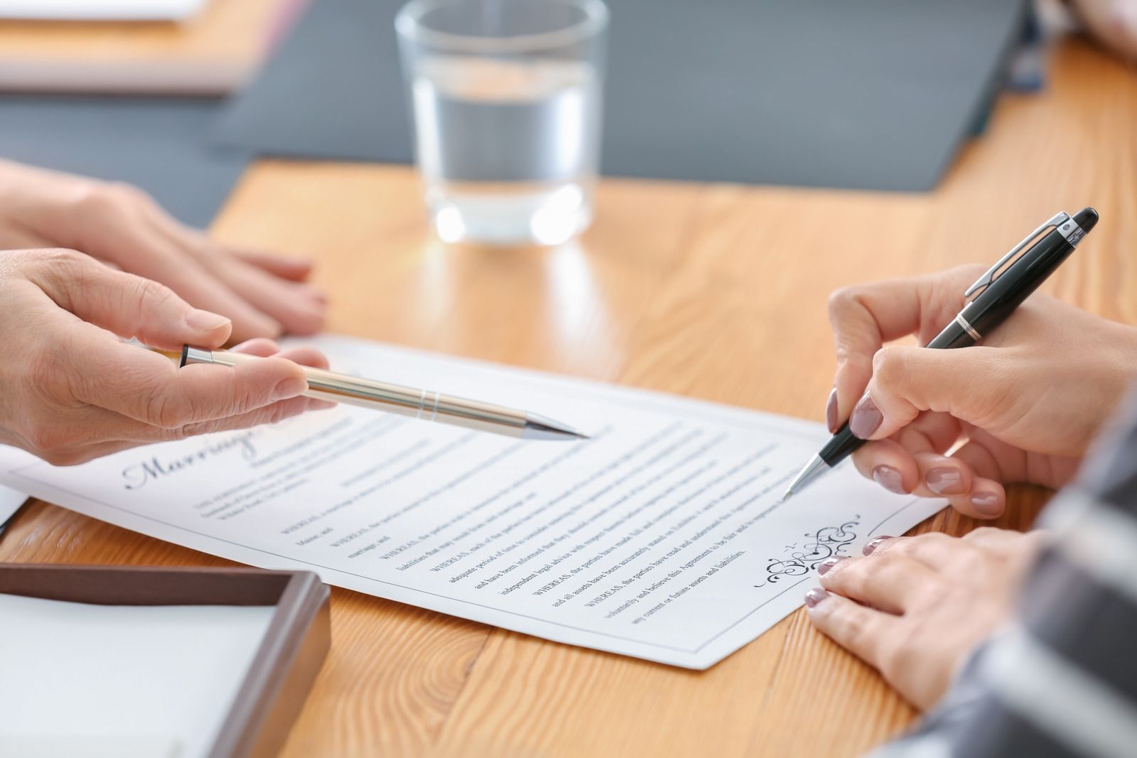 A person is signing a document with a pen on a wooden table.