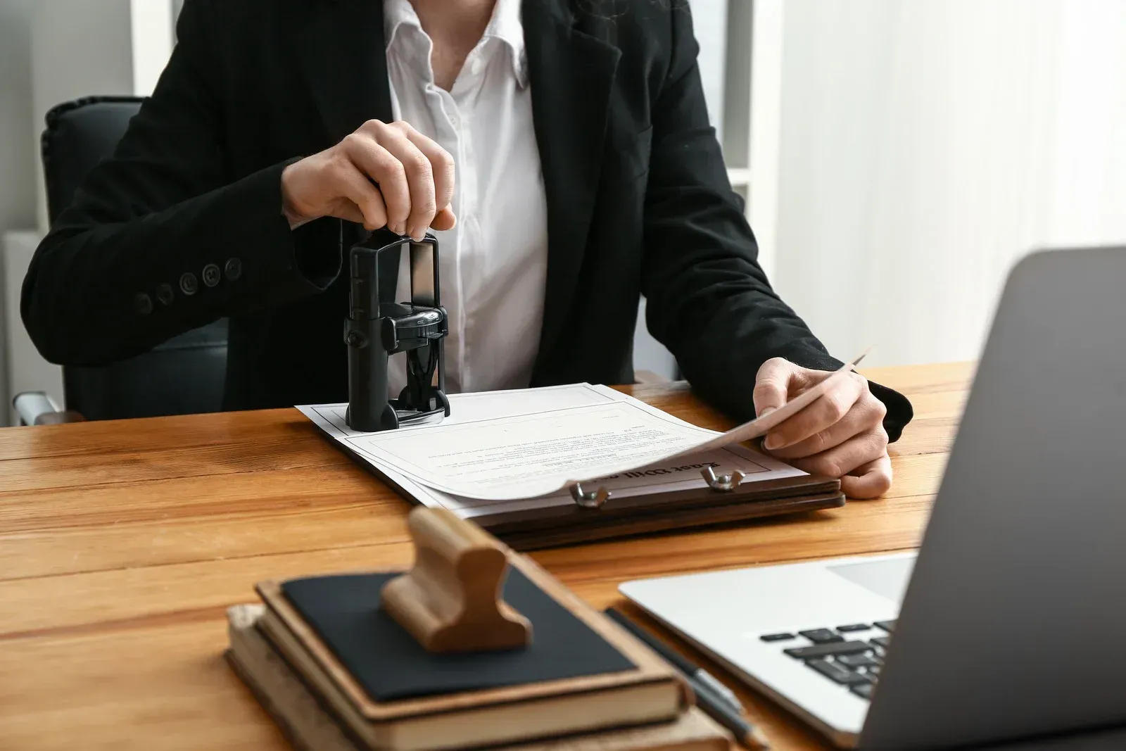 Person in suit stamps document at desk with laptop.