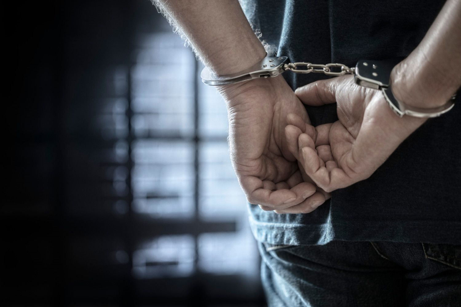 A man in handcuffs is standing in a dark room.