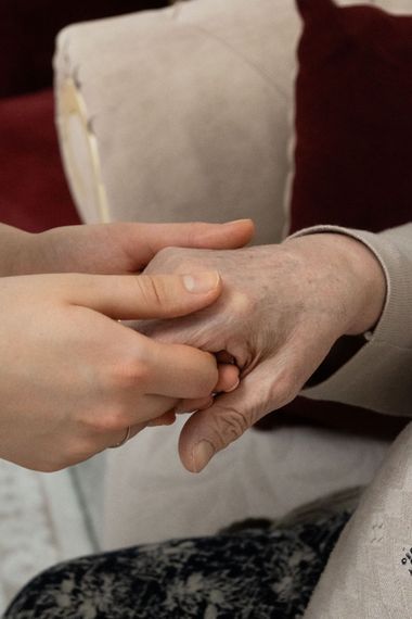 Dos manos que se toman suavemente una de la otra, con una silla blanca al fondo.