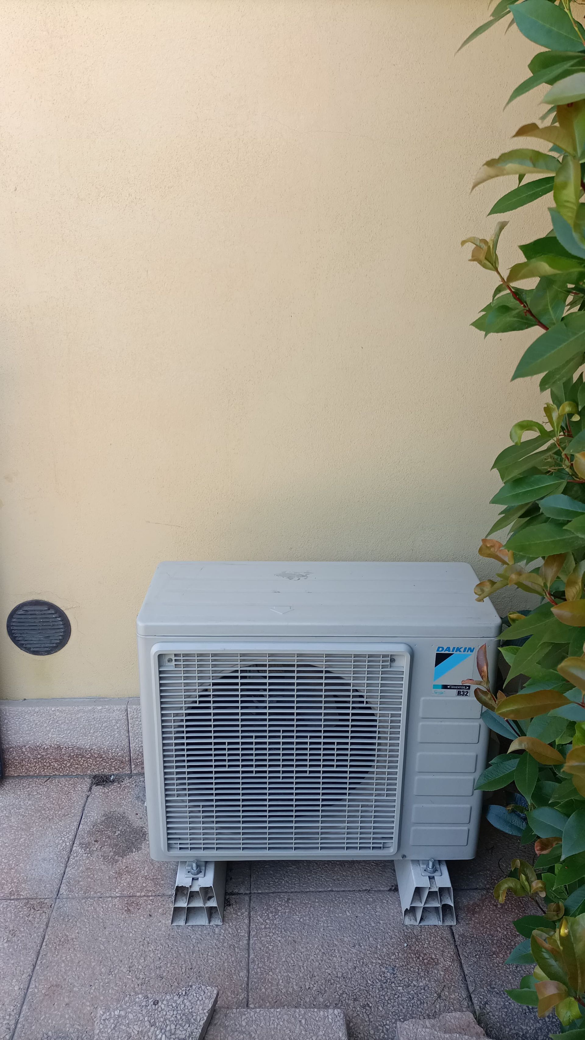 Un condizionatore bianco è posizionato su un patio, accanto a un muro giallo.