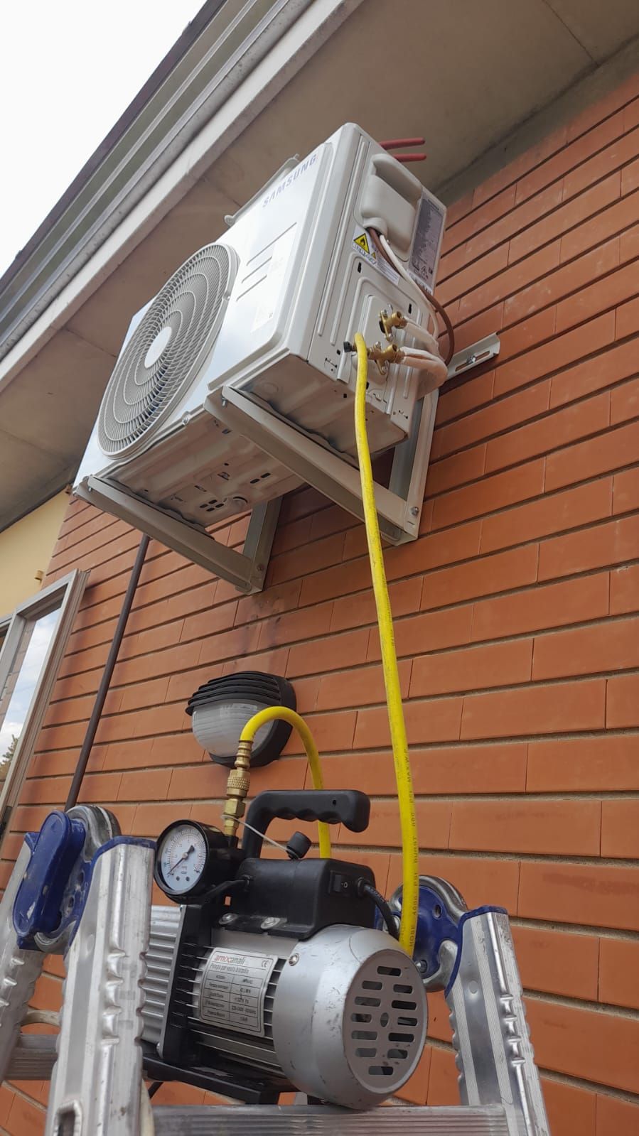 Un condizionatore d'aria viene installato su un muro di mattoni con una pompa a vuoto attaccata.