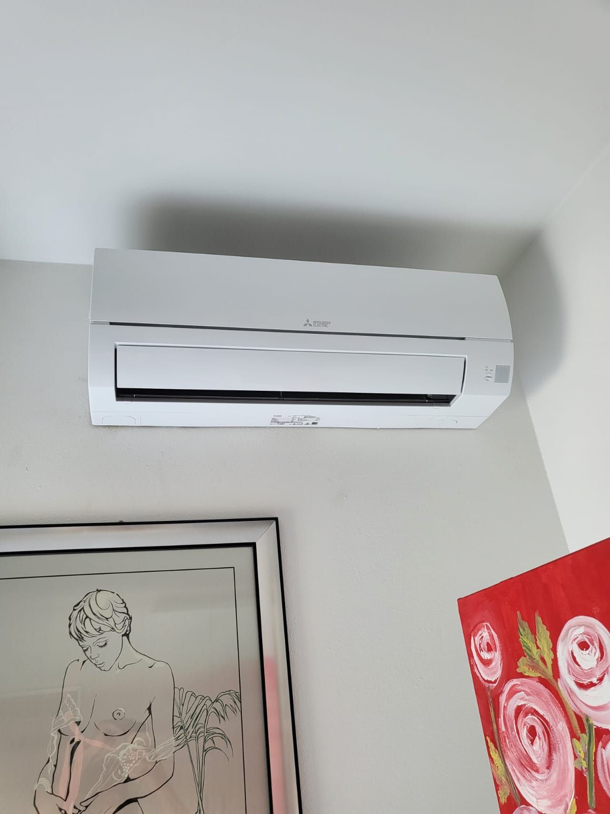 In una stanza, accanto a un quadro, è appeso al soffitto un condizionatore bianco.