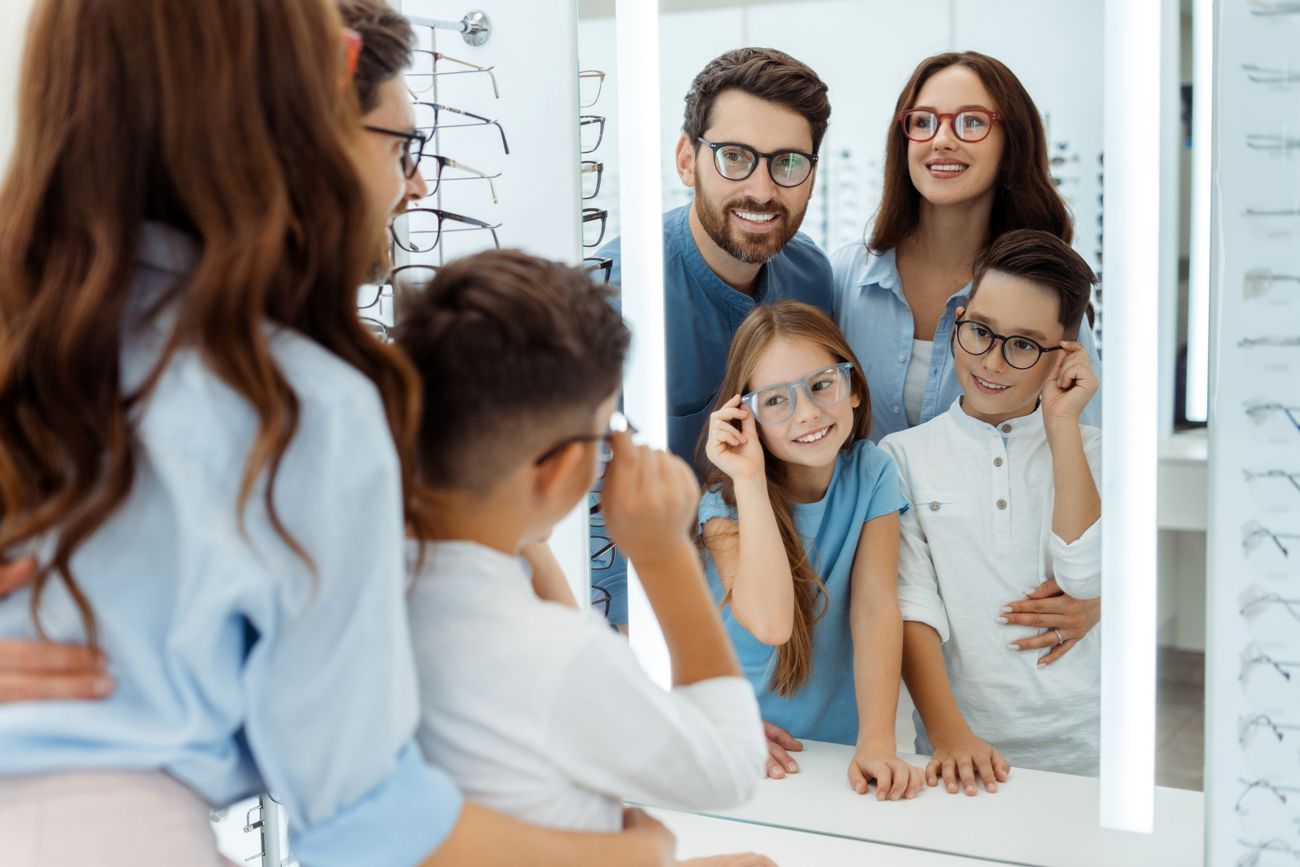 Happy parents and kids looking at a mirror in an optical store.