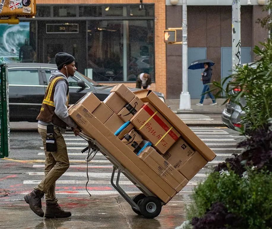 A Man Is Pushing A Cart Full Of Boxes Down A Street — Local & Country Removals in Helensvale, QLD