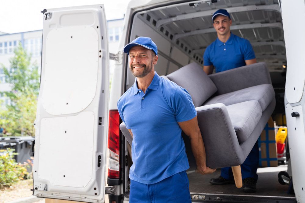 Two Men Are Carrying A Couch Out Of A Van — Local & Country Removals in Helensvale, QLD
