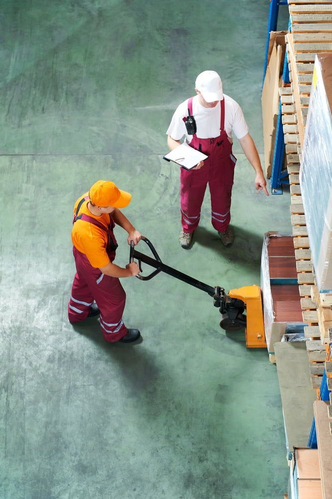 A Man Is Pushing A Pallet Truck In A Warehouse While Another Man Looks On — Local & Country Removals in Tweed Coast, NSW