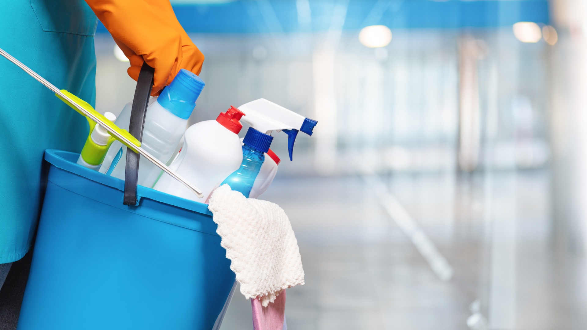 A person is holding a blue bucket filled with cleaning supplies.