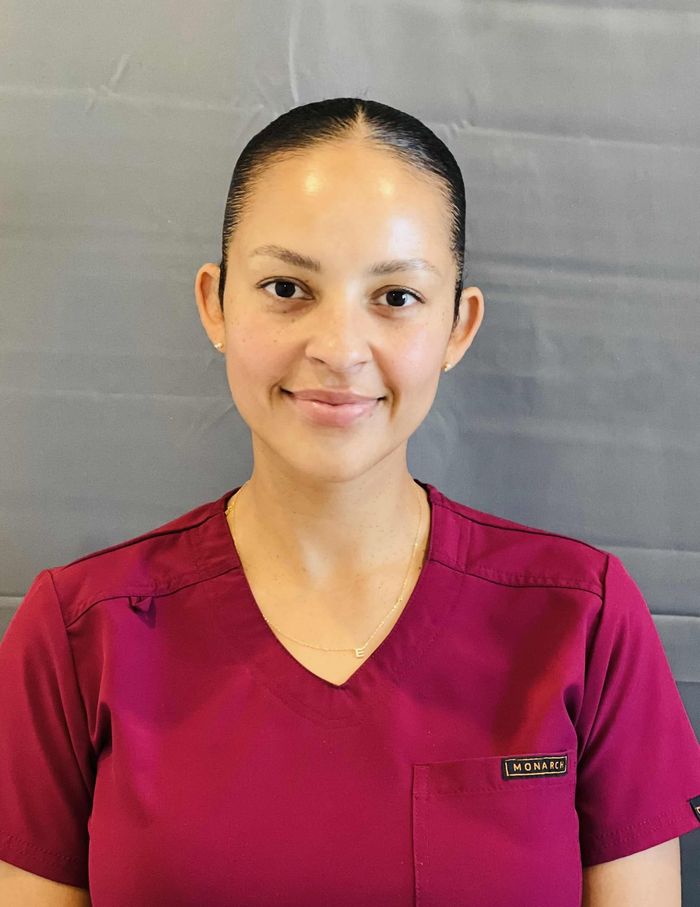 Woman in a burgundy scrub top smiling at the camera.