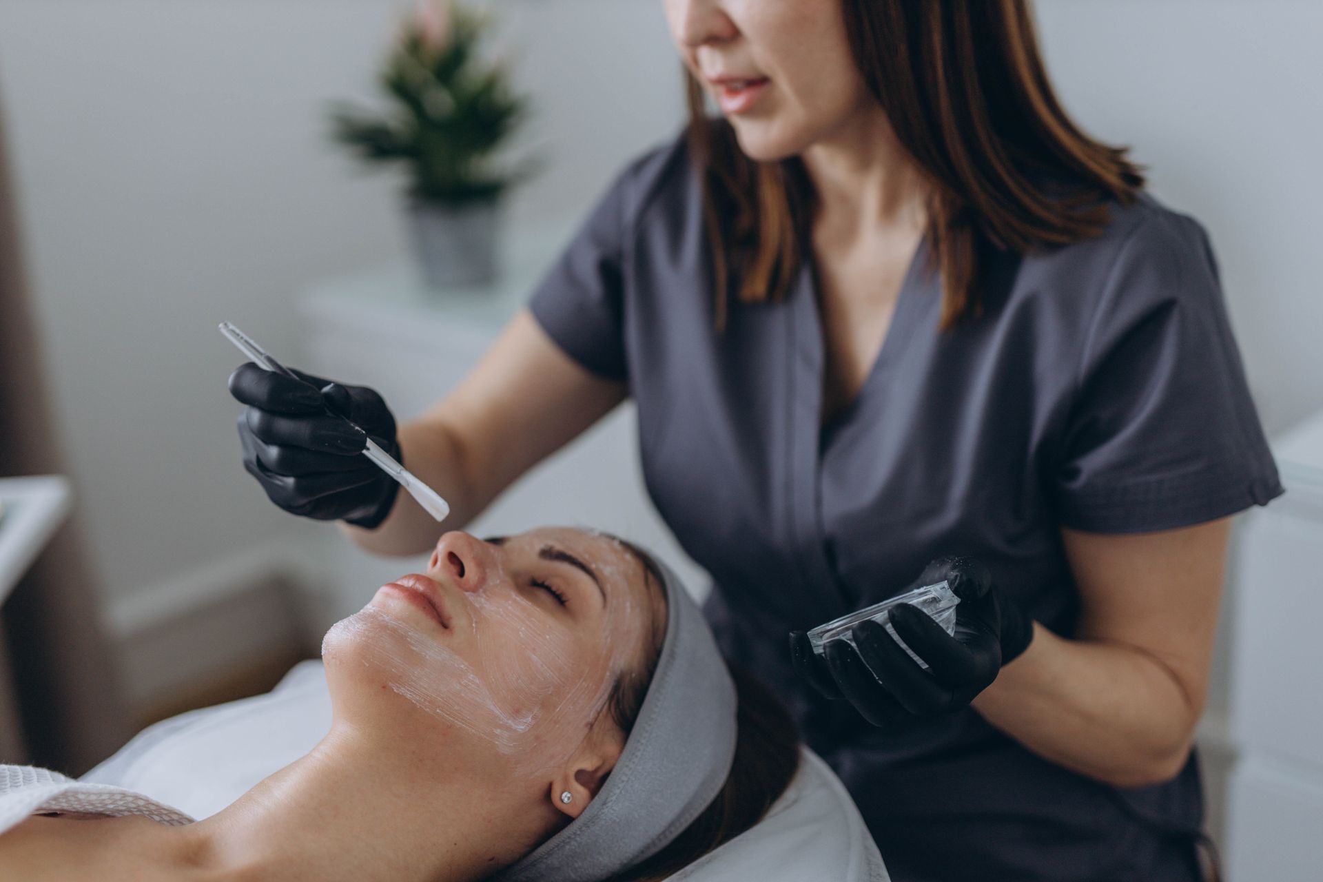 Aesthetician applying facial treatment with a brush to a client in a spa setting
