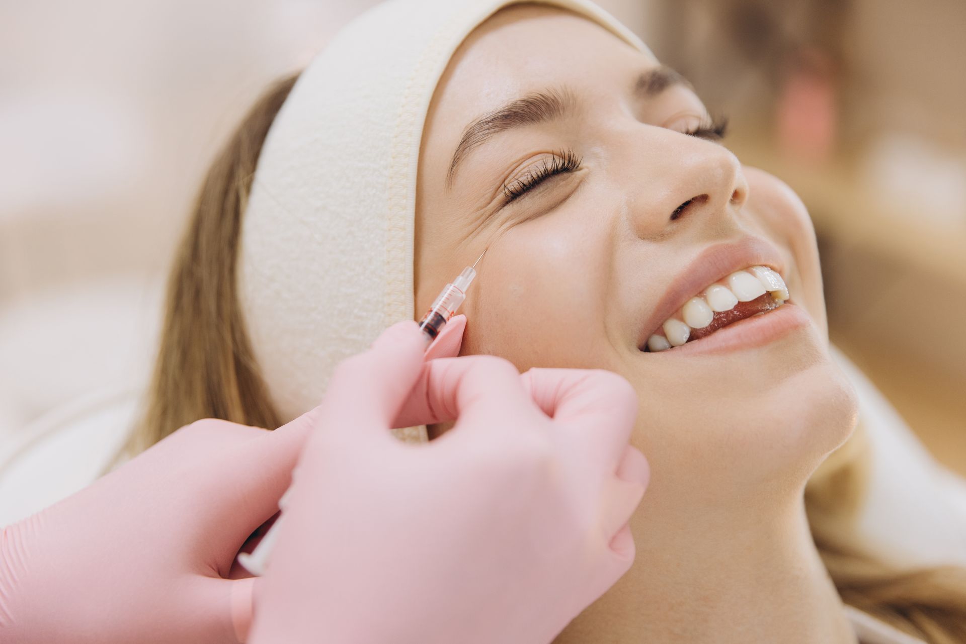 Hands in pink gloves applying makeup to a smiling woman’s eyebrow in a close-up salon setting