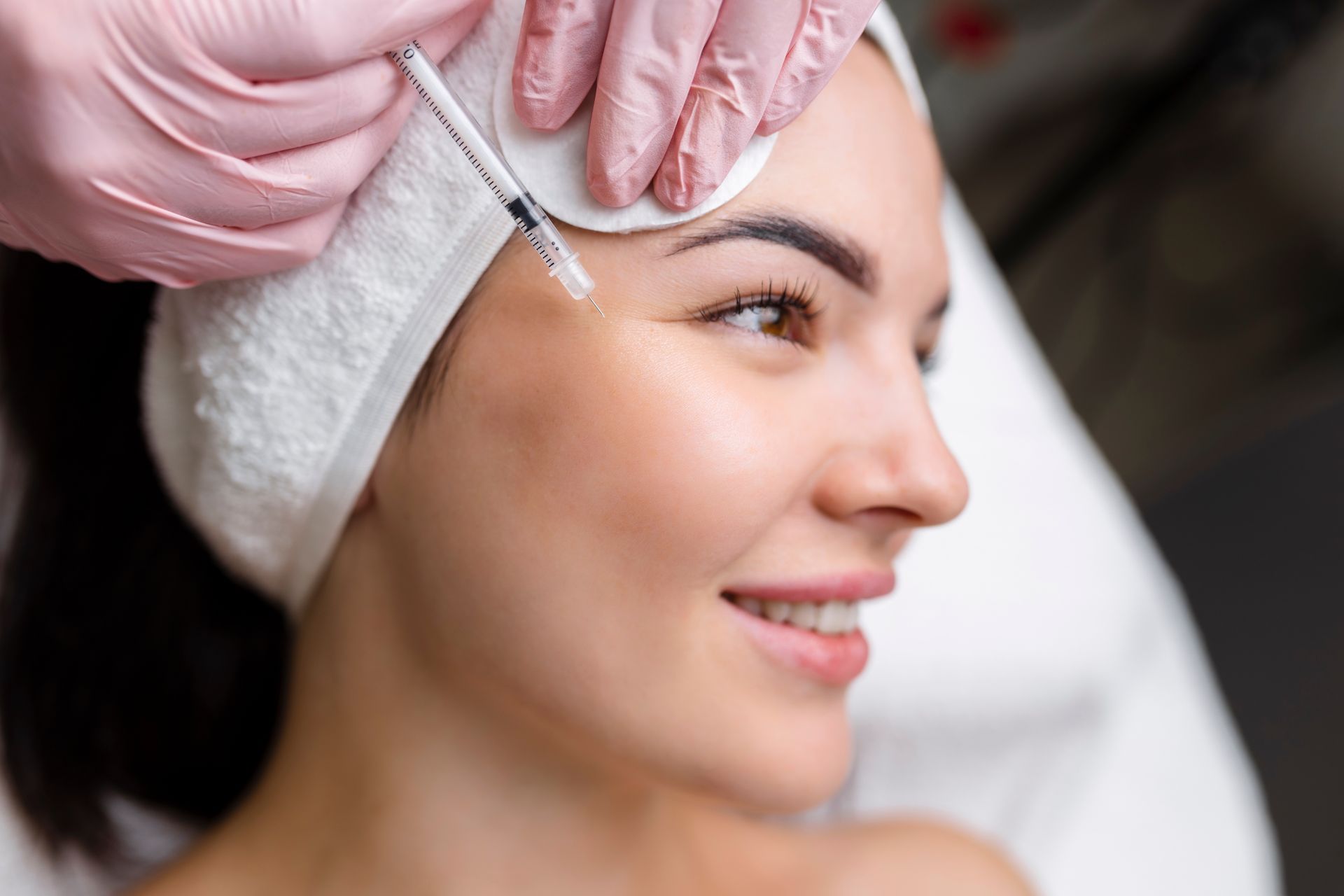 A woman receives a facial injection from a gloved practitioner in a spa setting