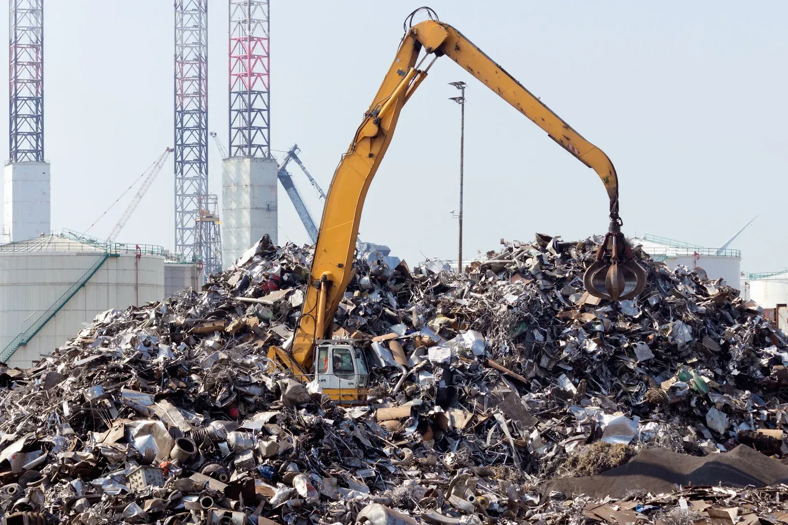 A yellow excavator is working on a pile of scrap metal.