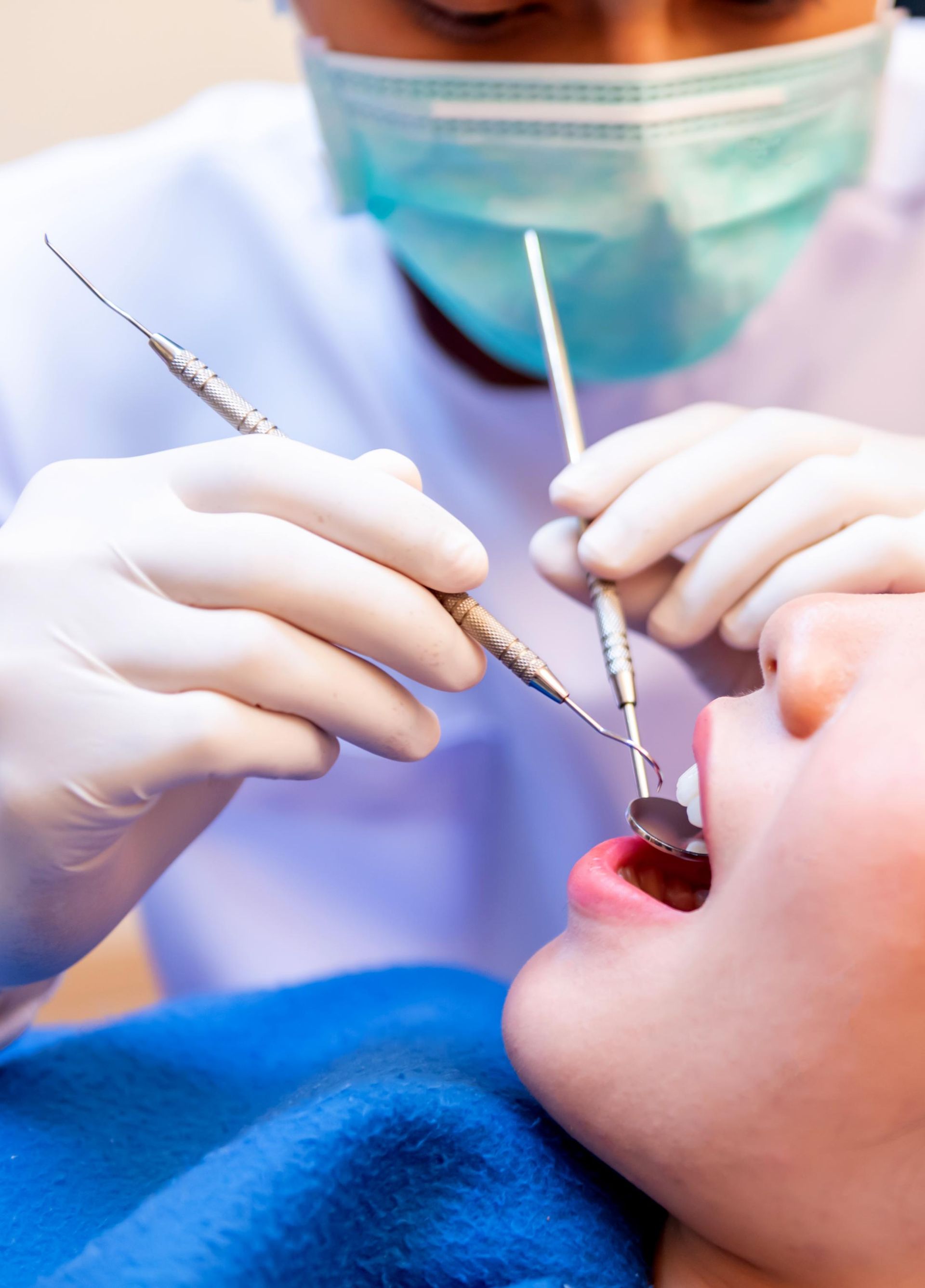 Dentist wearing gloves and mask examining a patient’s mouth with dental tools