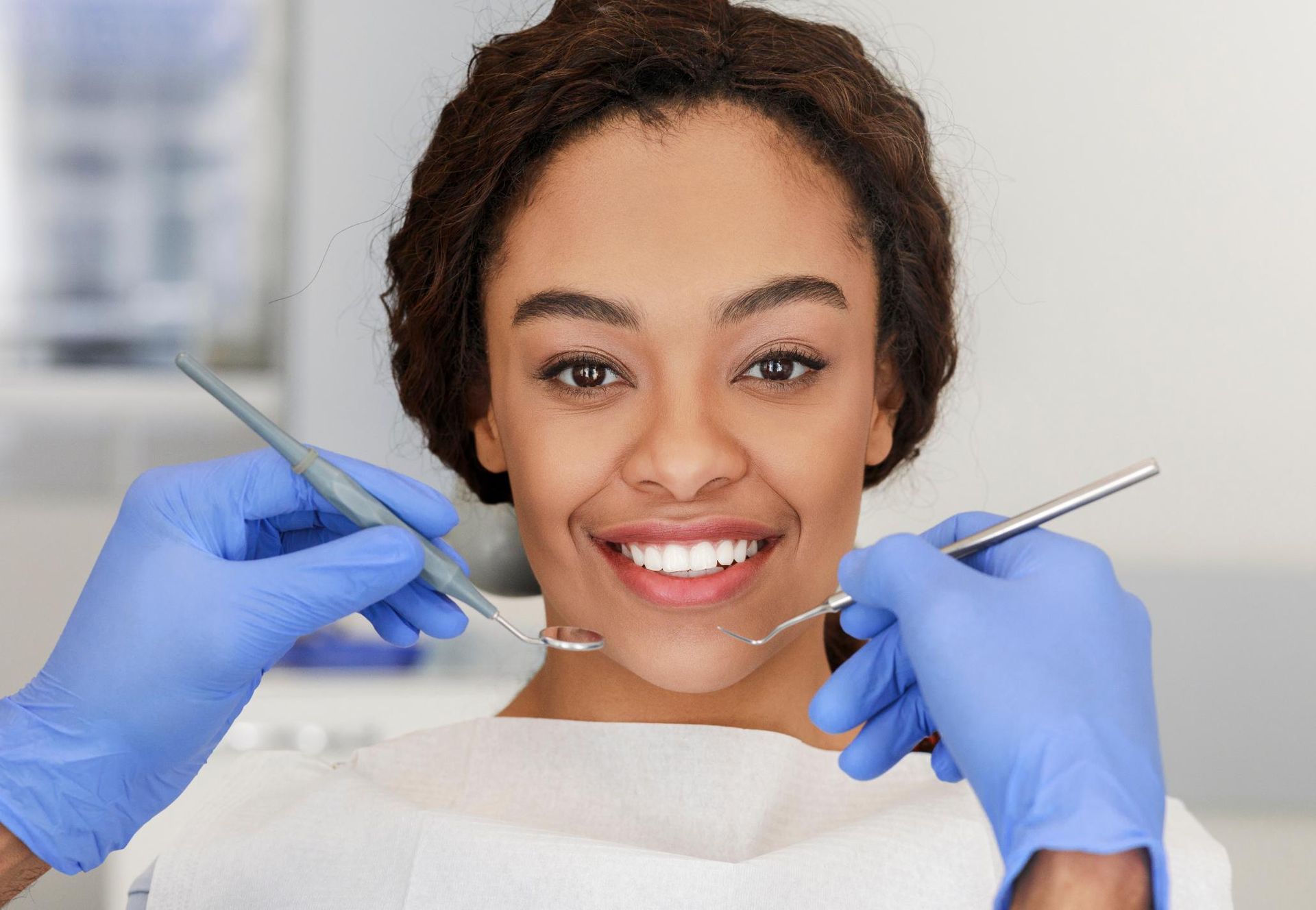 Smiling patient with dental tools and blue-gloved hands in a clinic chair