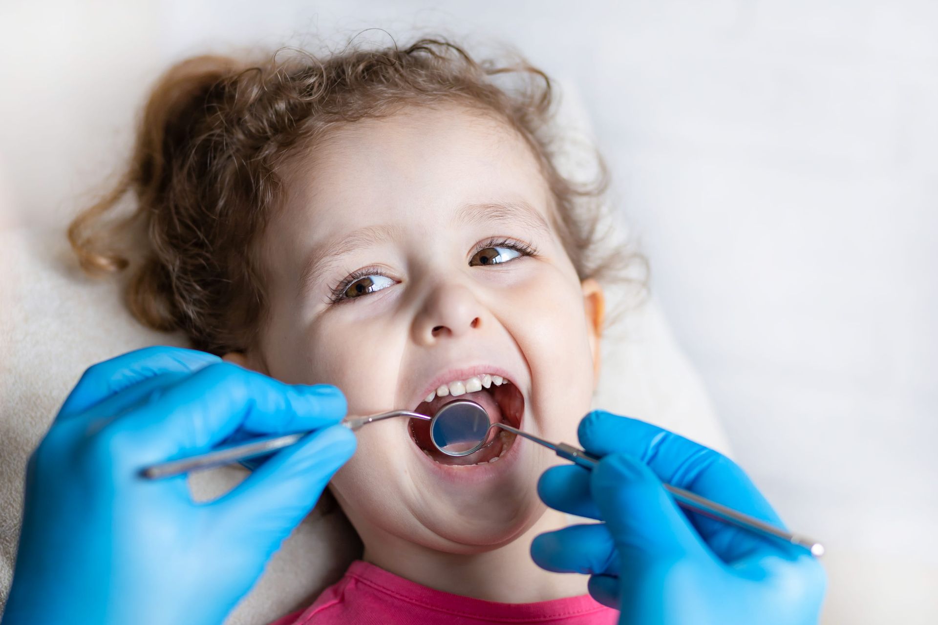 Dentist examining a child’s mouth with gloved hands and dental tools