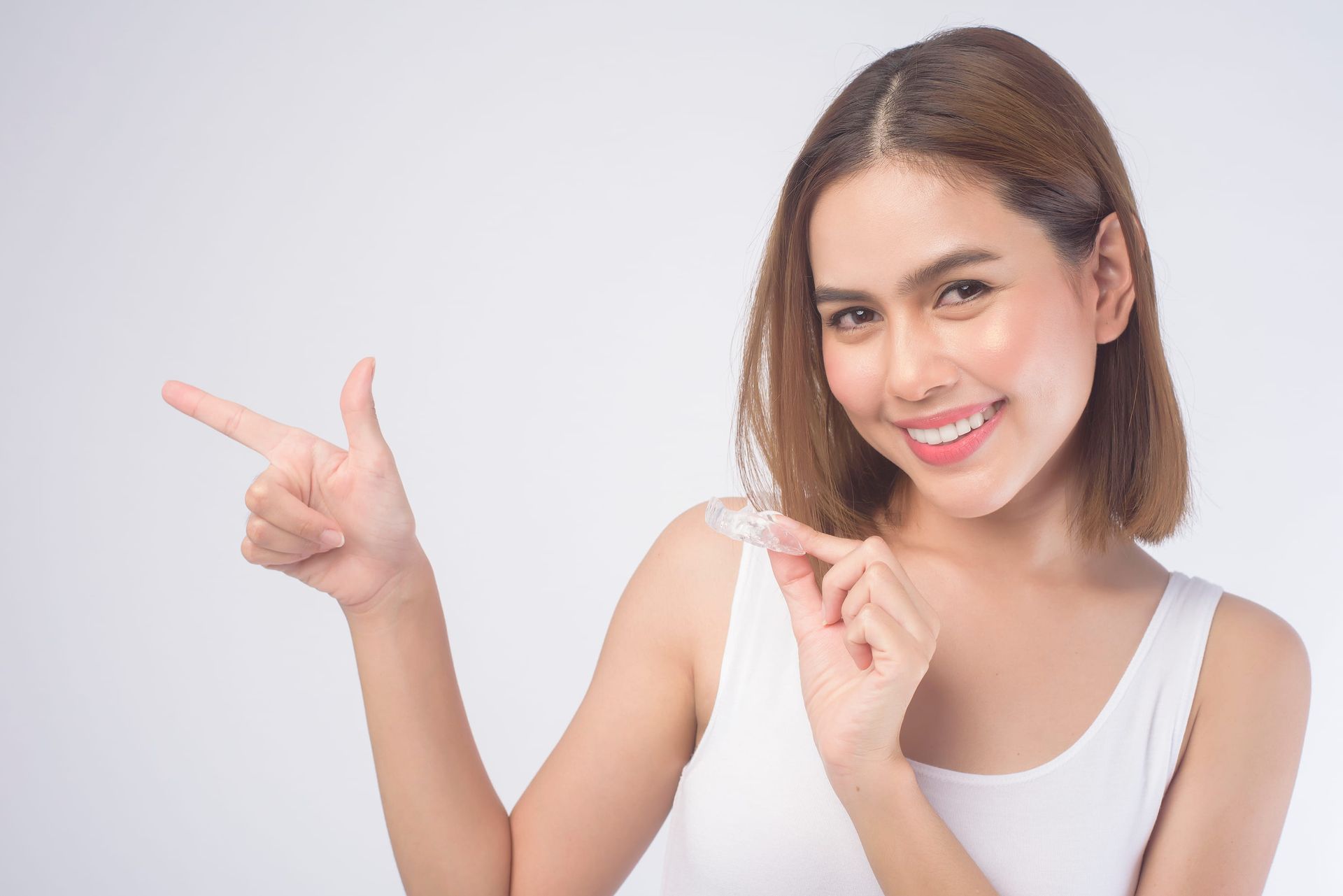 Smiling person in a white top pointing left on a plain background