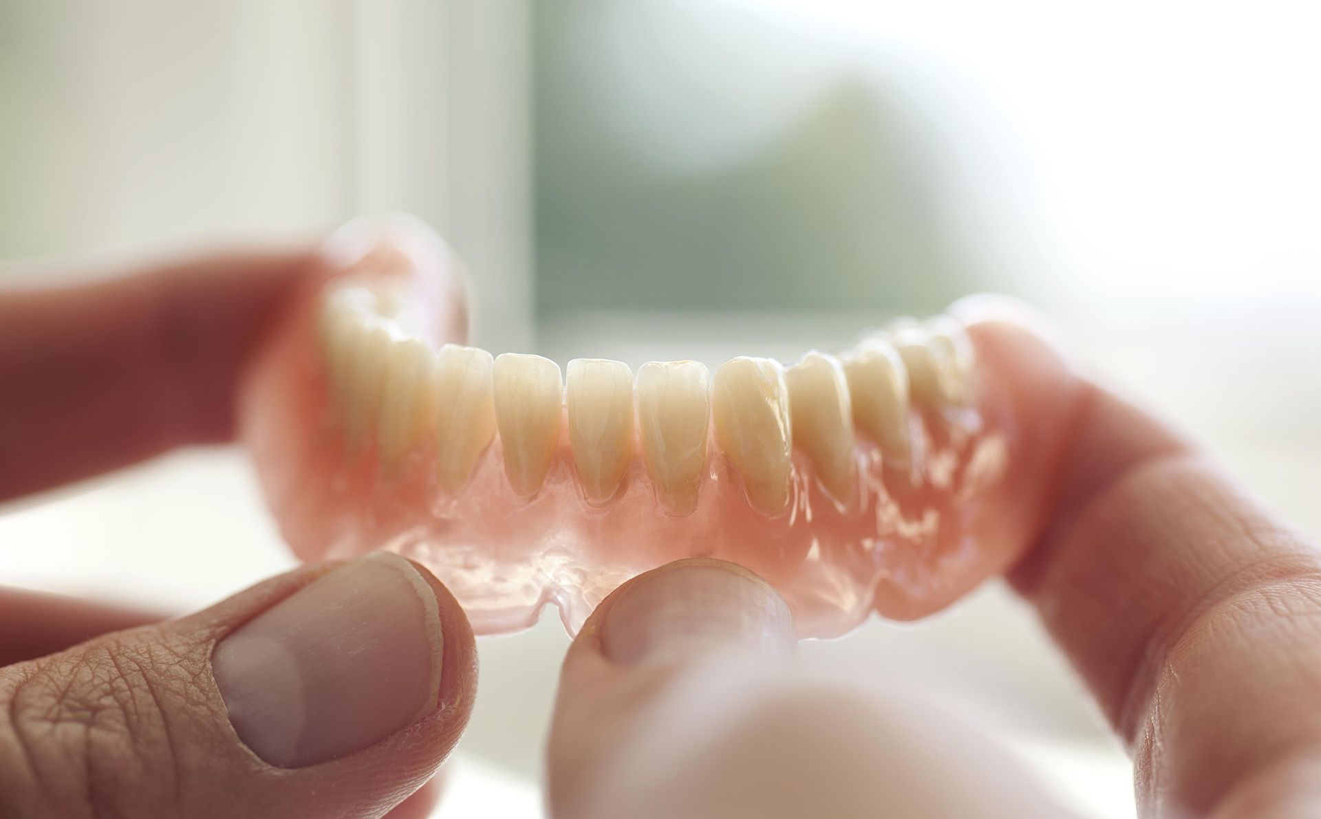 Hands holding a translucent pink dental retainer against a bright background
