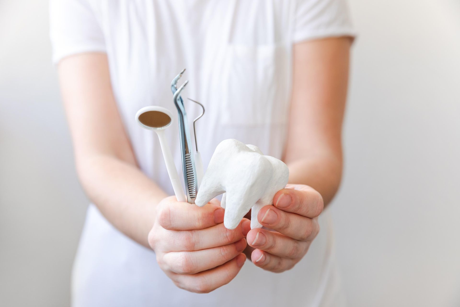 Hands holding dental tools and a tooth model against a white background