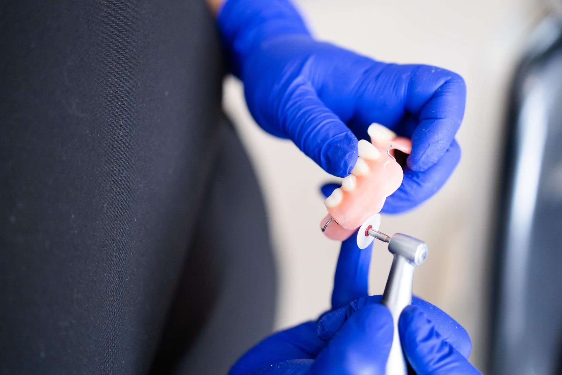 Gloved hands using a nail drill on a client’s fingernails