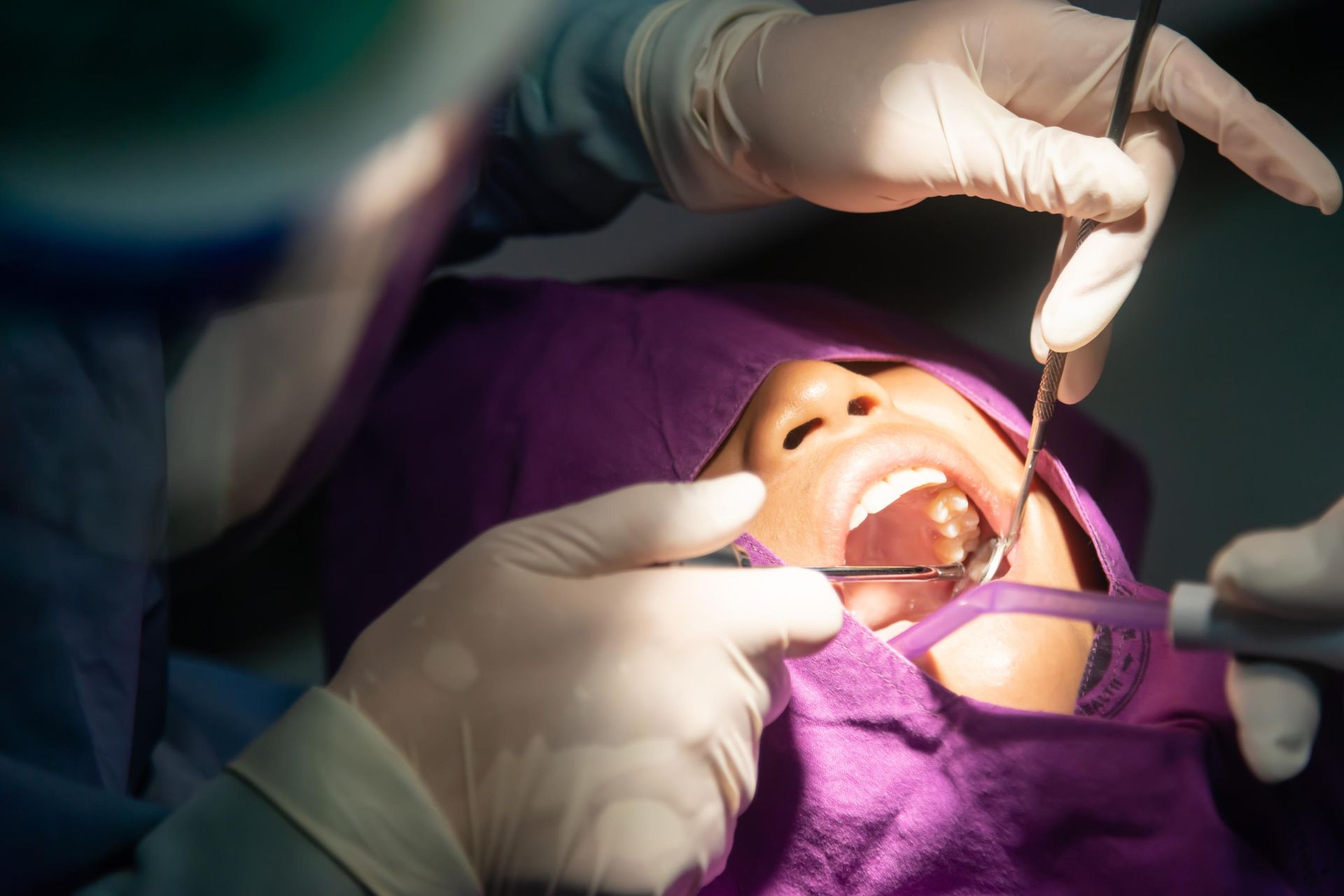 Dentist performing a procedure on a patient’s open mouth with gloved hands and dental tools