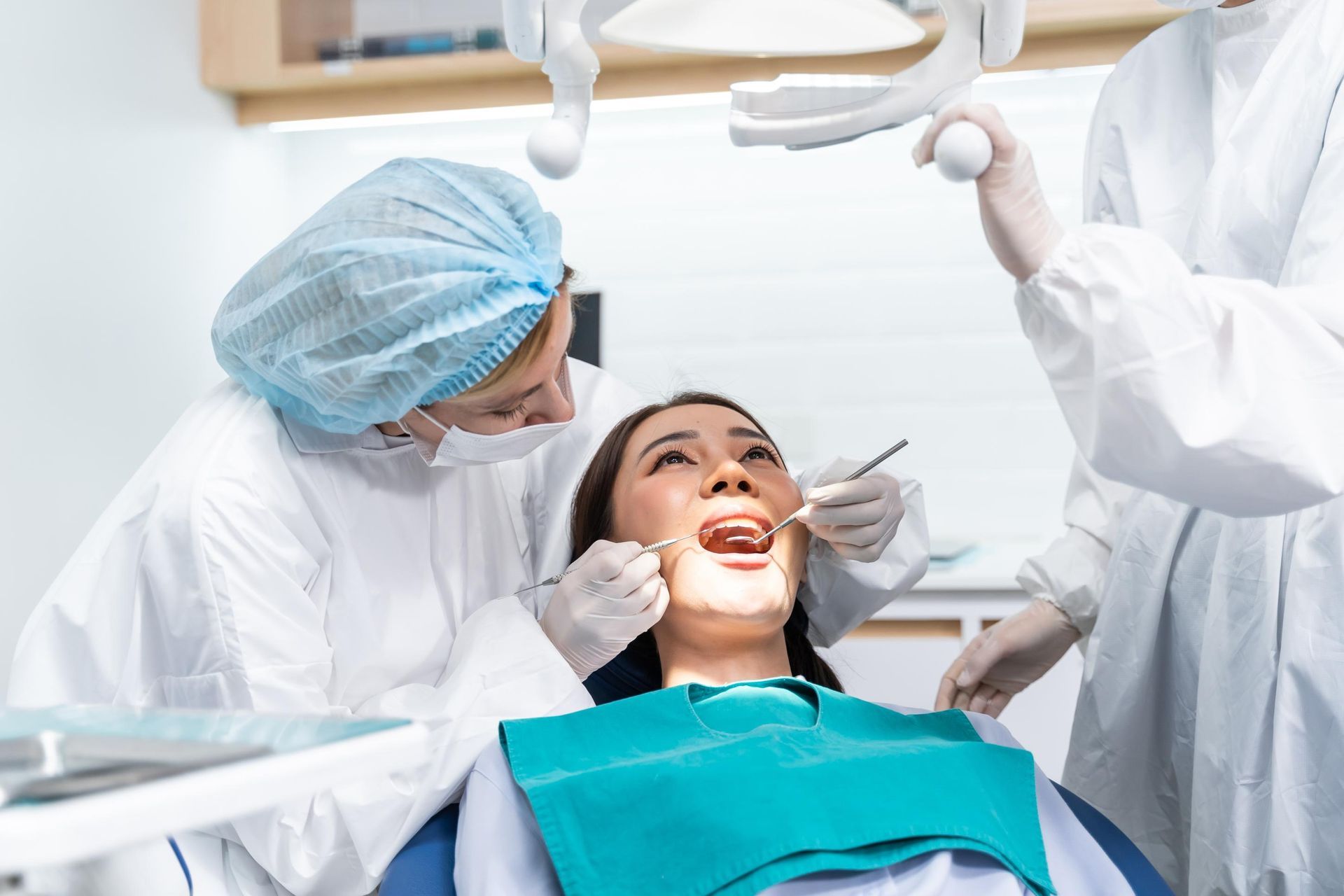 Dentist treating a smiling patient in a bright clinic, with dental tools and a blue cap visible