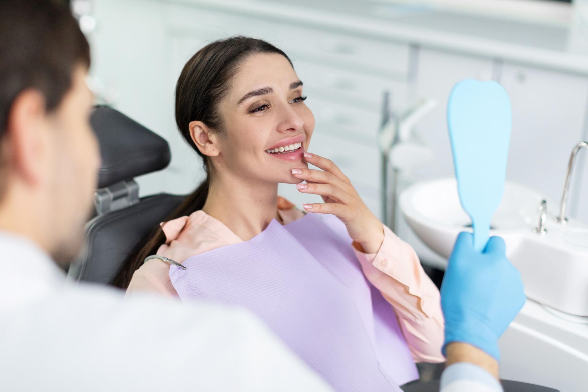 Dentist and patient smiling during a dental checkup, with a blue dental mirror visible