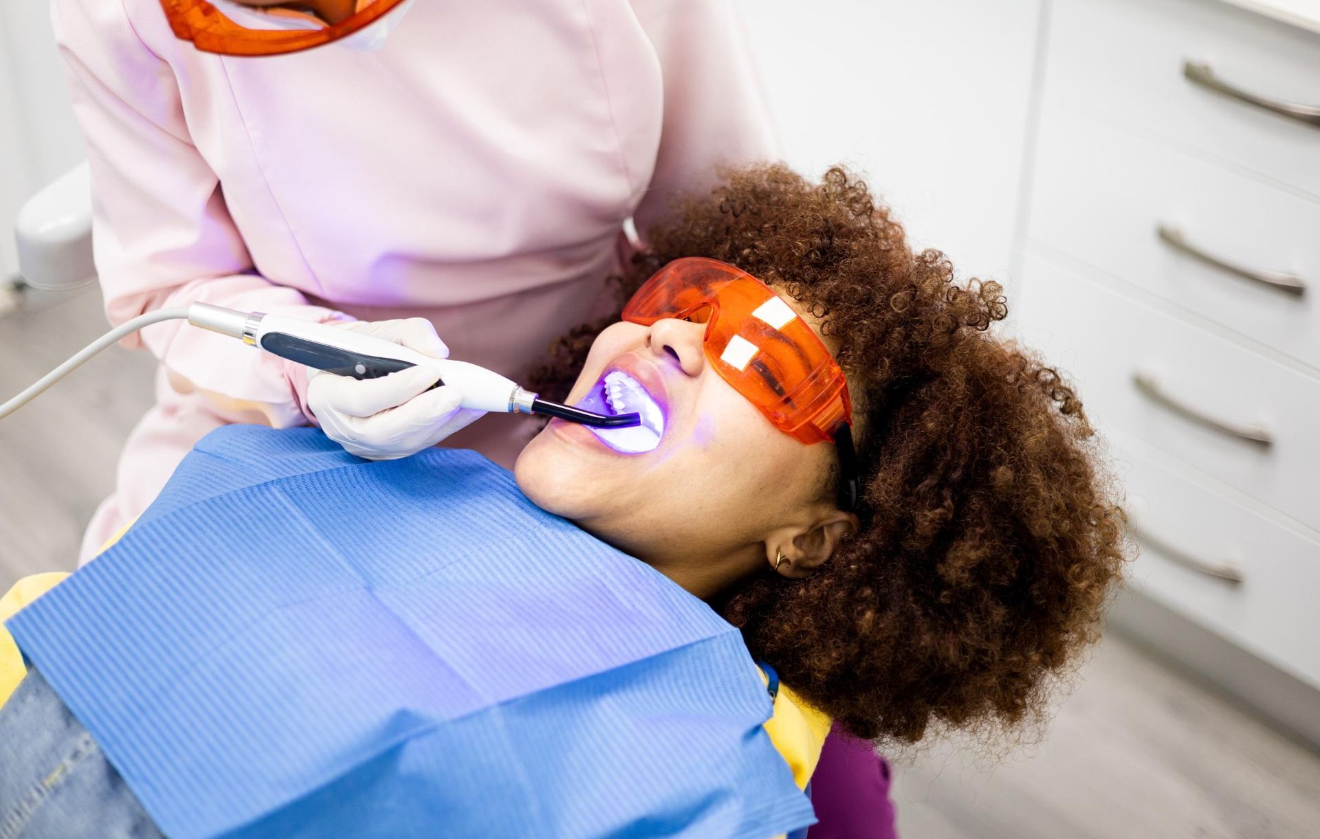Dentist using a drill on a patient wearing orange protective glasses in a dental chair