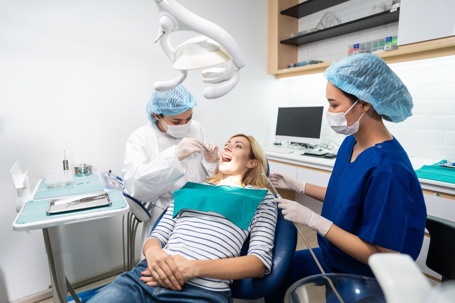 Dental team treating a smiling patient in a modern clinic, with blue scrubs and dental equipment.