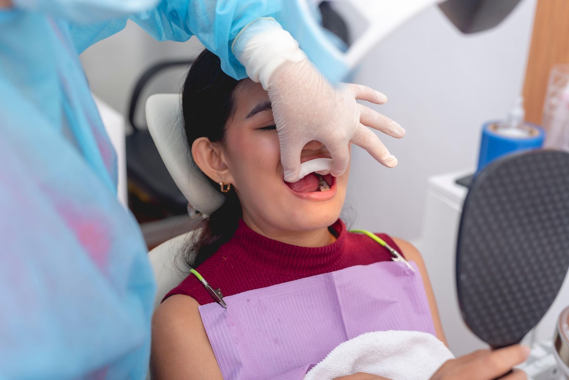 Dentist examining a patient’s mouth with a gloved hand in a dental chair