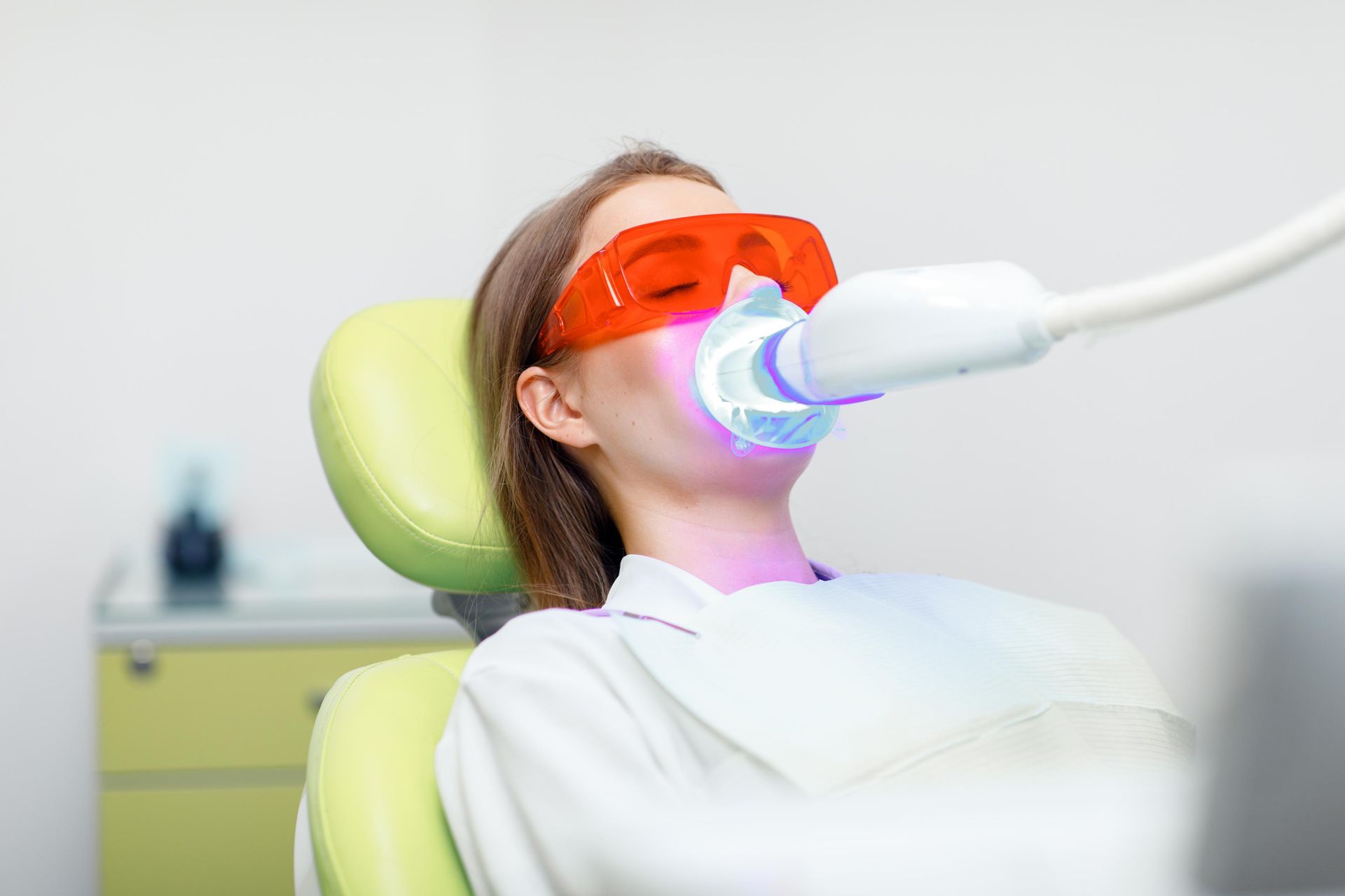 Patient wearing orange protective glasses during laser dental treatment in a clinic chair