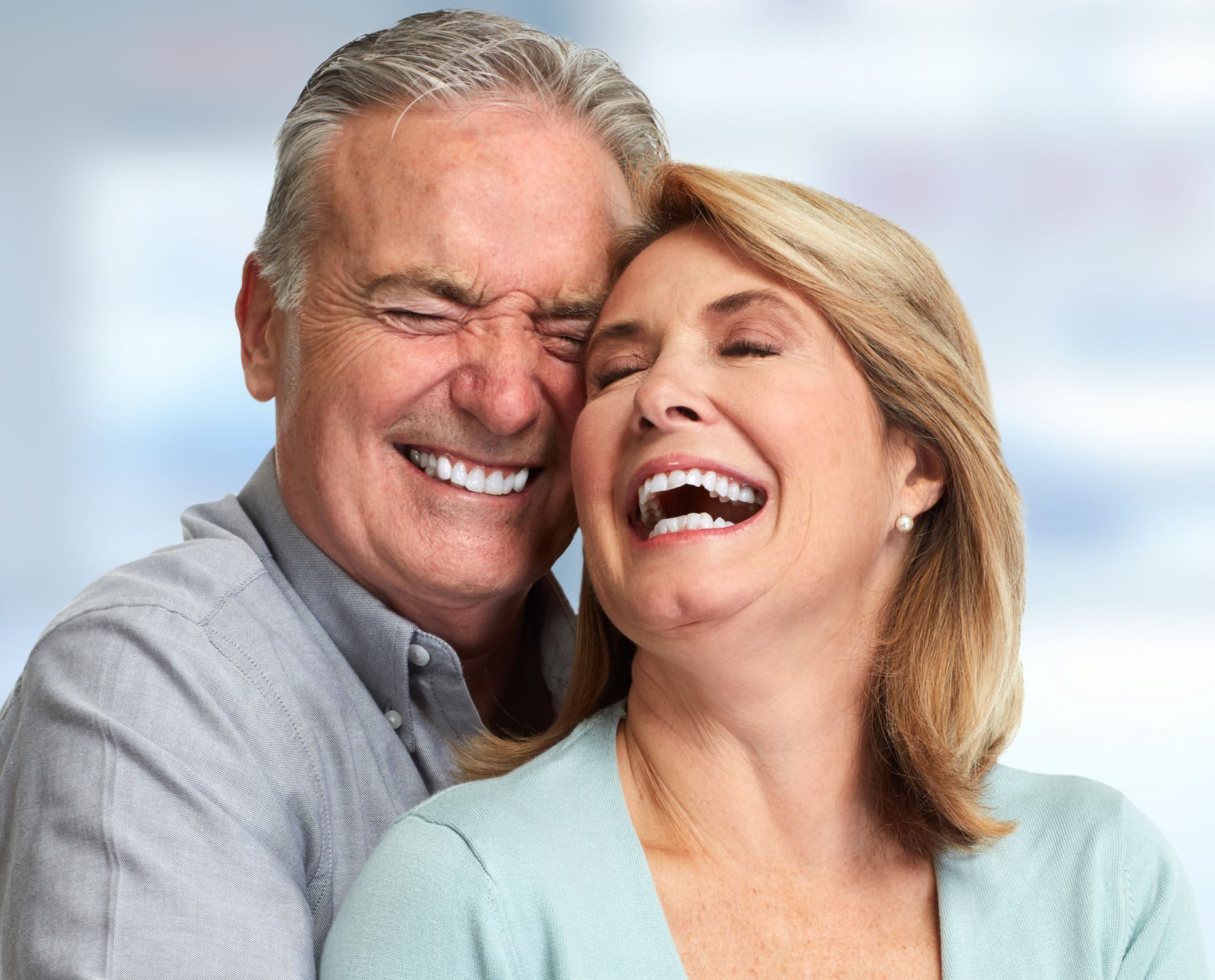 Smiling couple embracing closely, laughing against a light blue background.