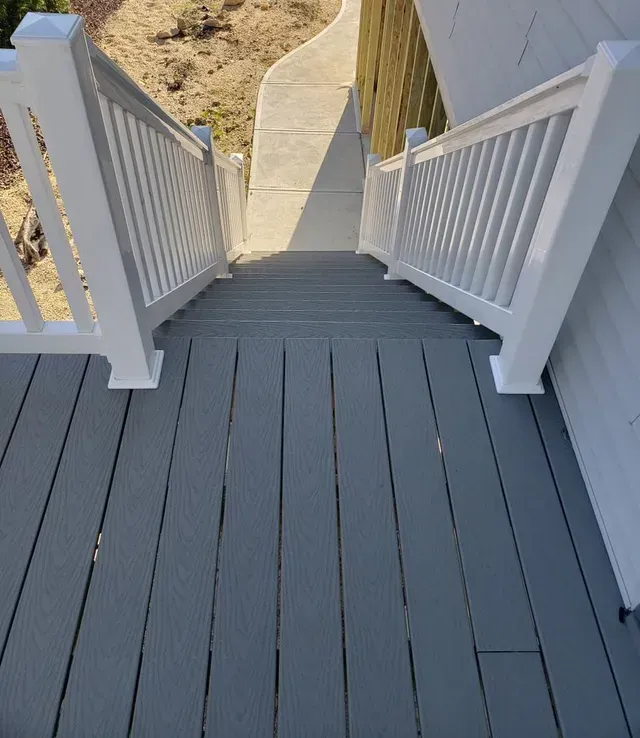 White porch stairs with railings leading down to a sandy yard and concrete path