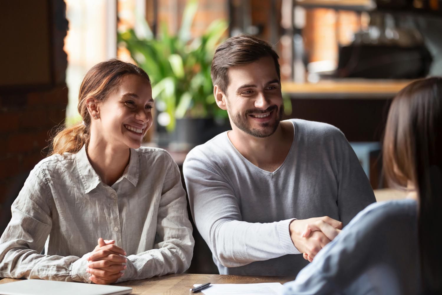Two people smiling at a table in a bright meeting room, speaking with someone across from them