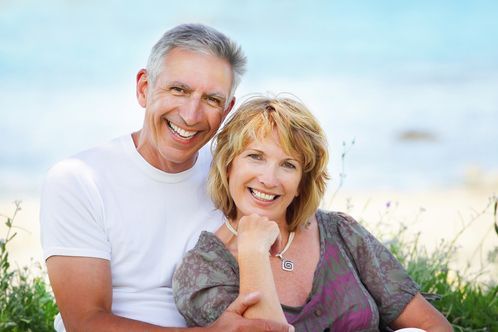 Smiling couple embracing outdoors by the ocean. Man in white shirt, woman in floral top.