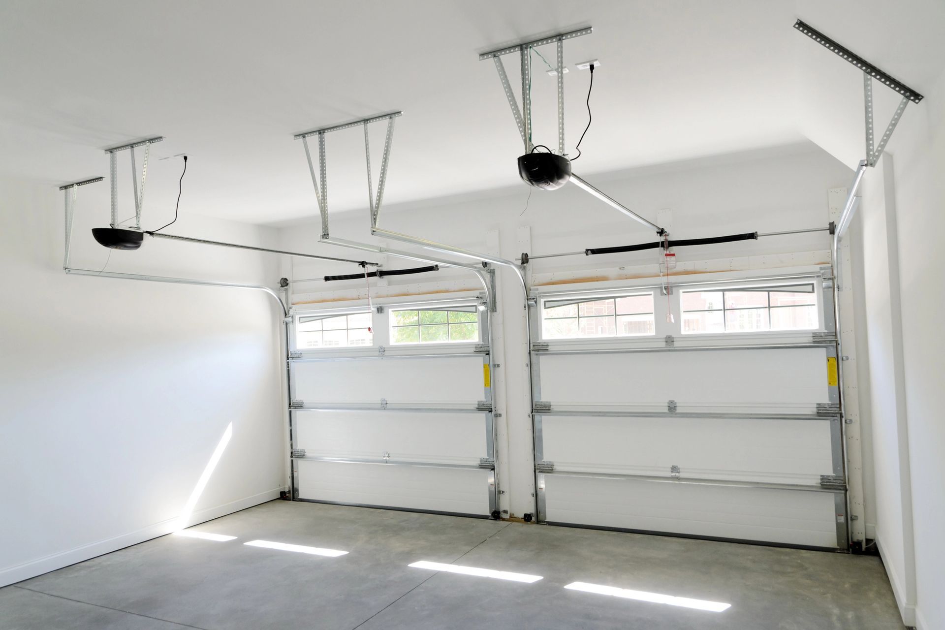 Empty white garage interior with two overhead doors and ceiling-mounted openers