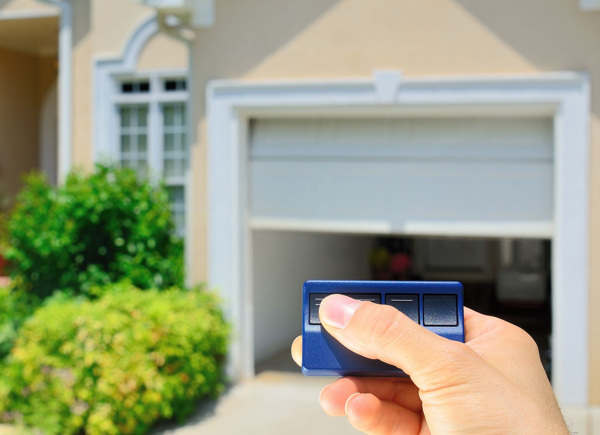 Hand holding a garage door remote in front of a suburban house and garage