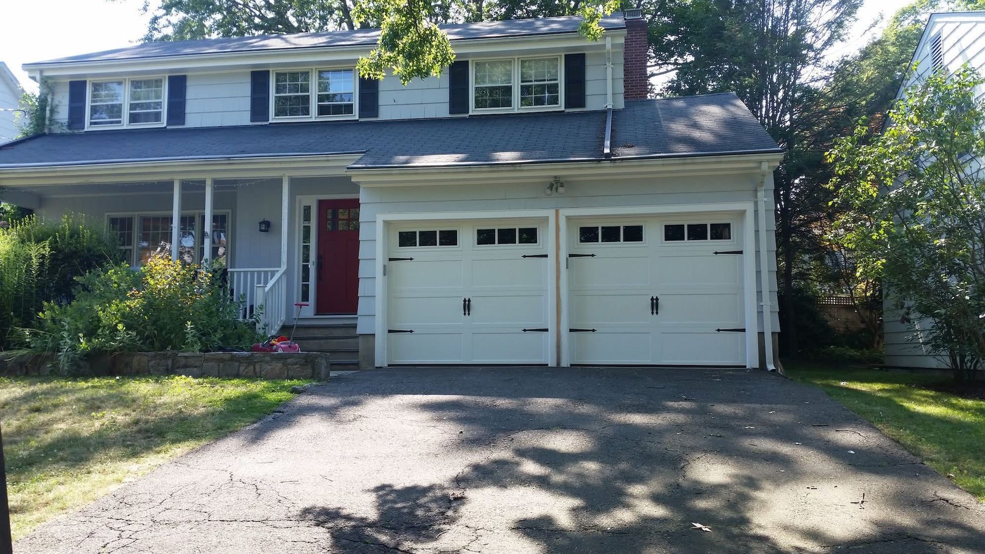Two-story suburban house with a red front door and double garage, viewed from the driveway.