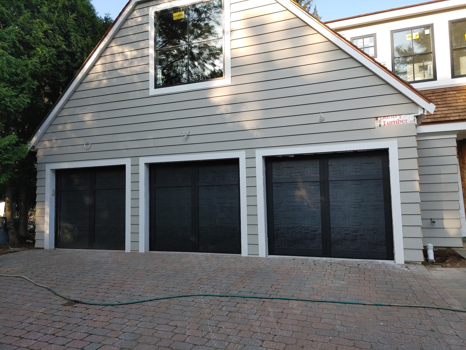 Three black garage doors on a light gray house with a peaked roof and brick driveway