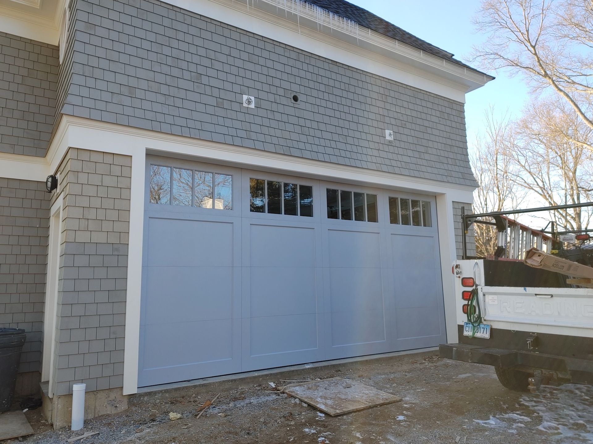 Gray garage with a large paneled door and small windows beneath a shingled exterior wall