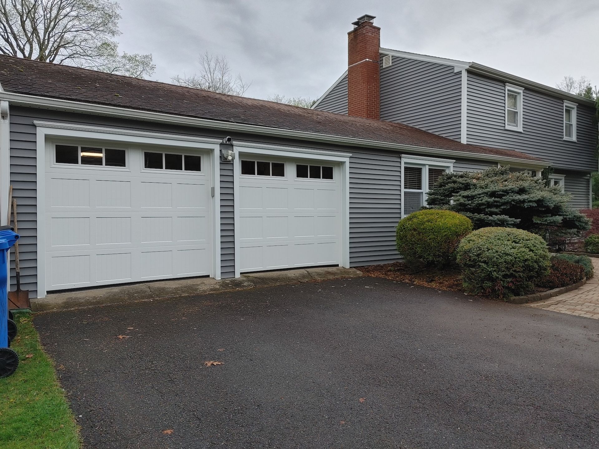 Suburban house with two white garage doors, gray siding, and a driveway in front