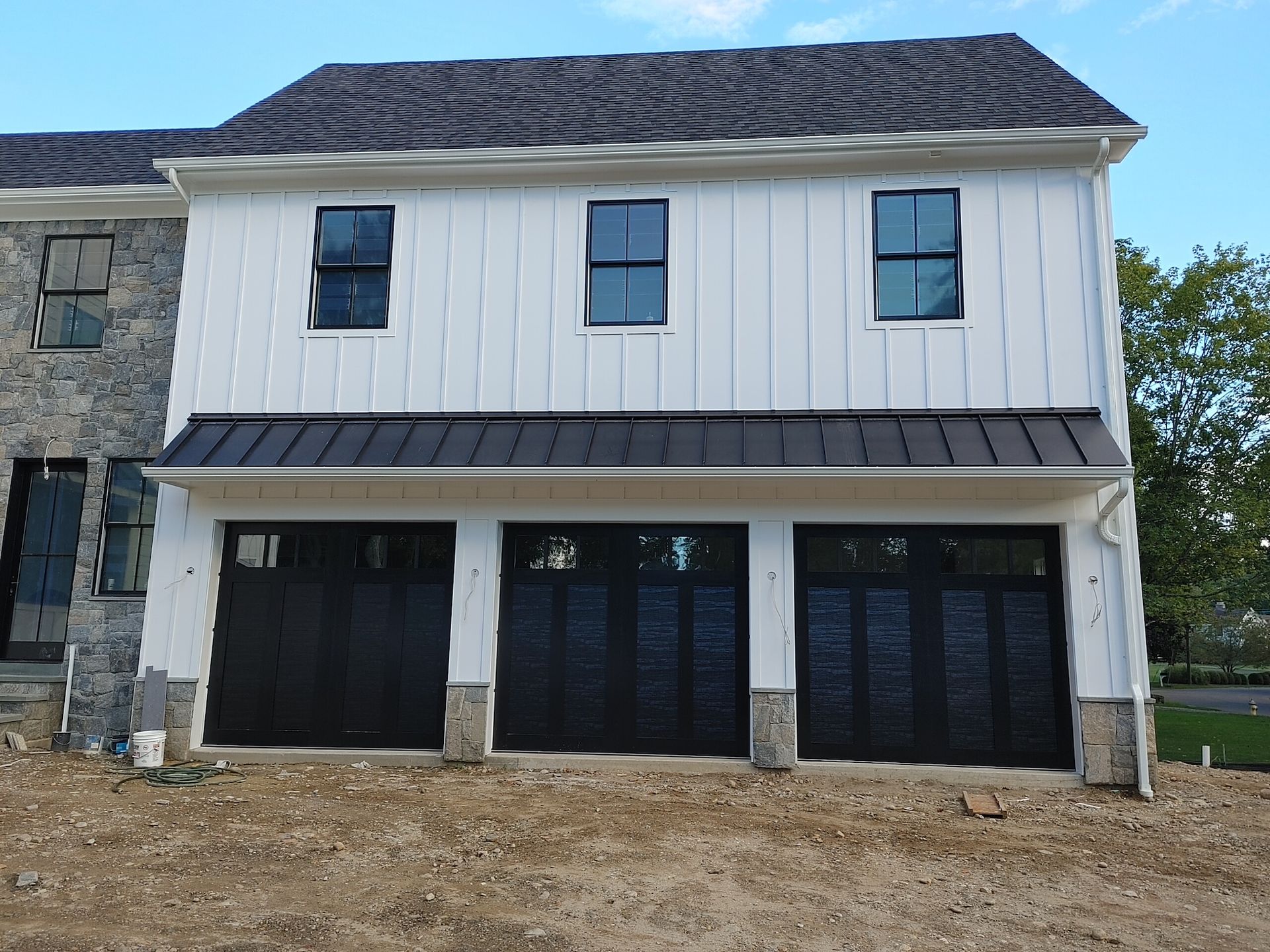 Two-story house with white siding, black doors, and a stone exterior on the left side