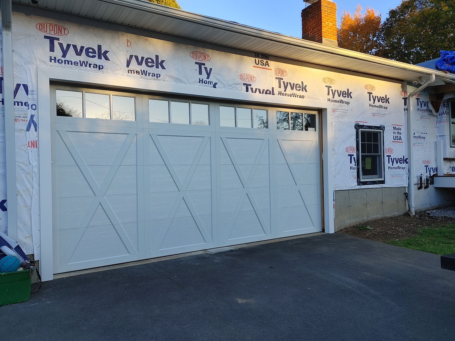 White garage with double doors, Tyvek house wrap, and a small front window on a paved driveway.