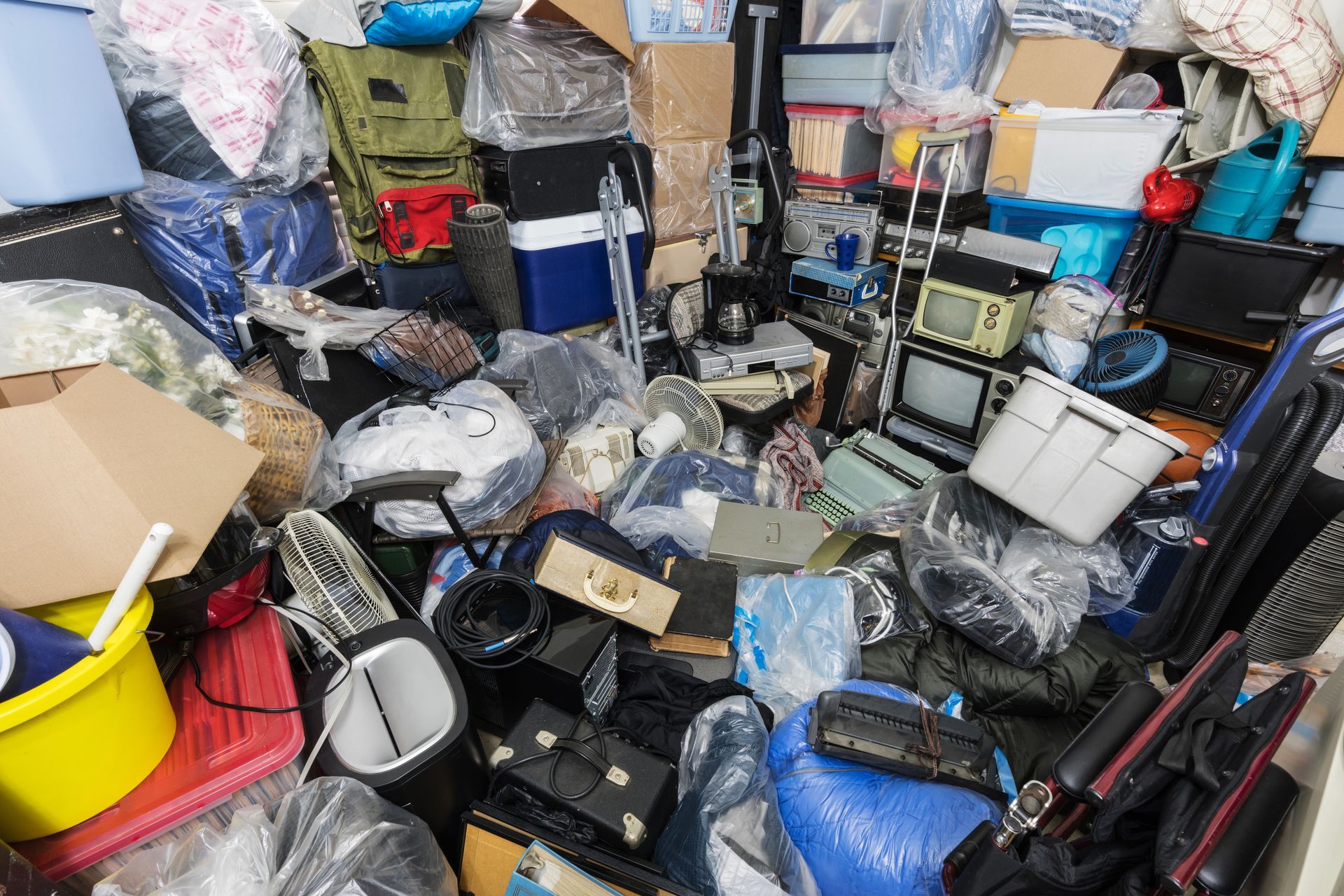 Cluttered room filled with stacked instruments, bags, and equipment in a messy storage area