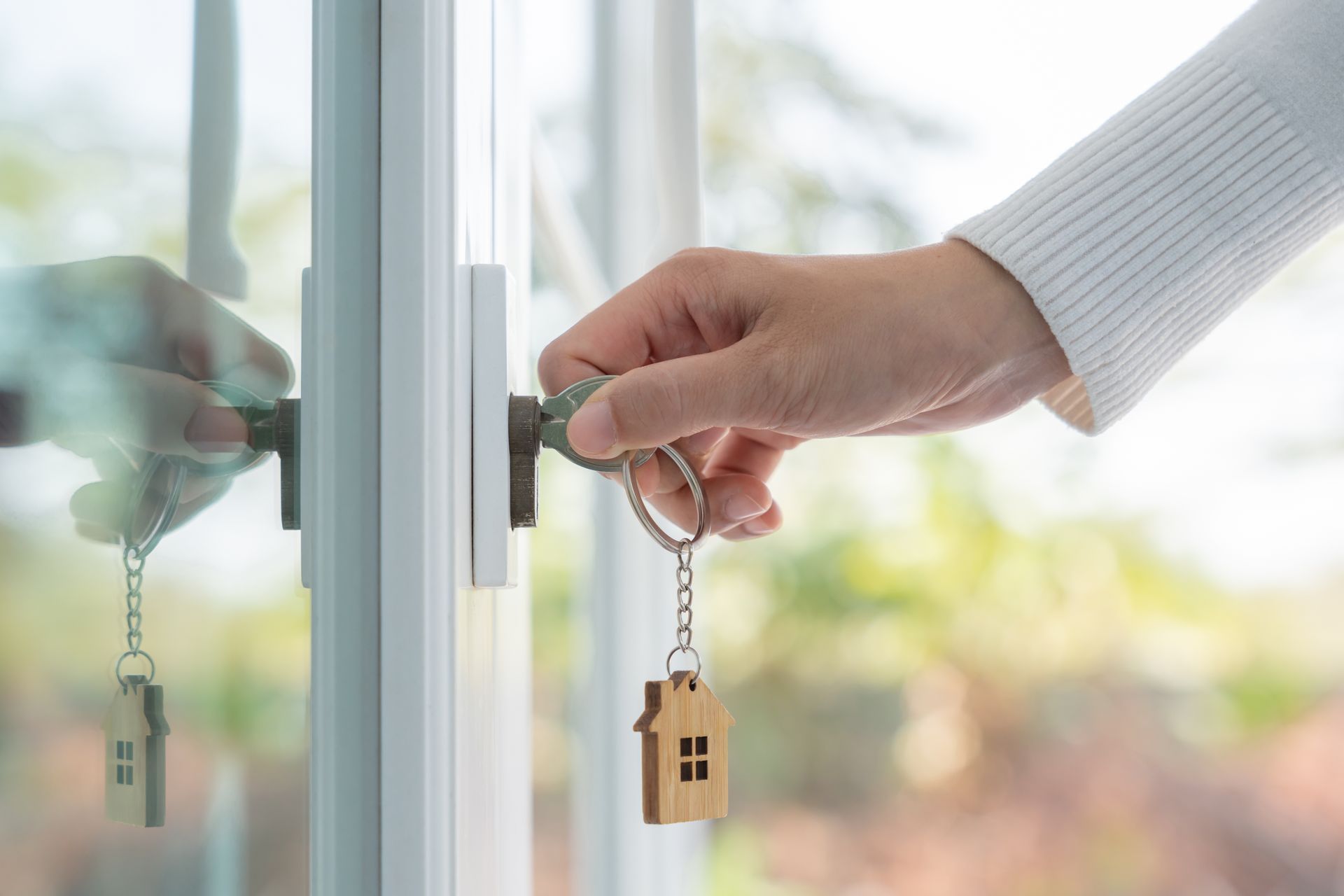 Hands holding house keys near a door handle, with a bright window in the background